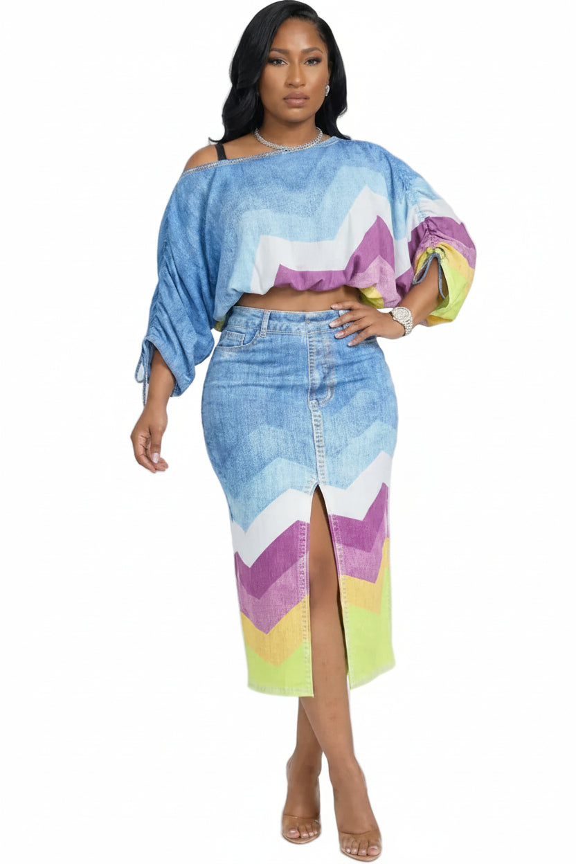 A woman modeling a matching two-piece set featuring a cropped off-the-shoulder top and a high-slit midi skirt, both in a blue denim-like fabric with a colorful chevron pattern of purple, pink, yellow, and white.