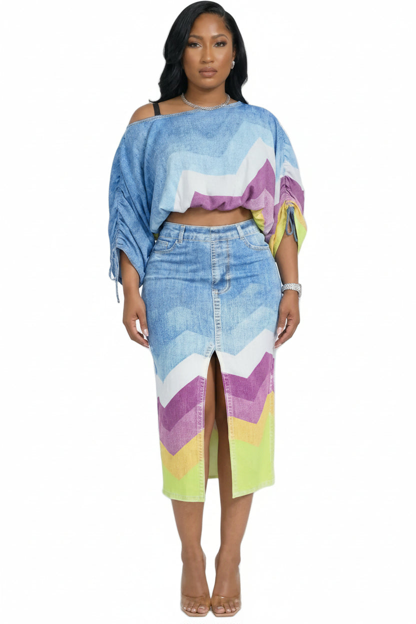 A woman modeling a matching two-piece denim set with a colorful chevron pattern in shades of blue, purple, pink, yellow, and green, set against a plain light gray studio background.