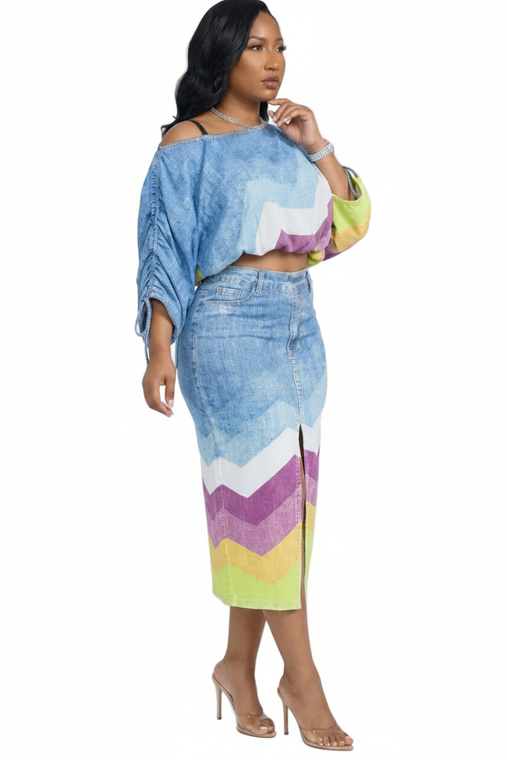 A woman modeling a matching two-piece outfit featuring a cropped off-the-shoulder top and a high-waisted pencil skirt, both in a blue denim-like fabric with a colorful chevron pattern in purple, white, yellow, and green.