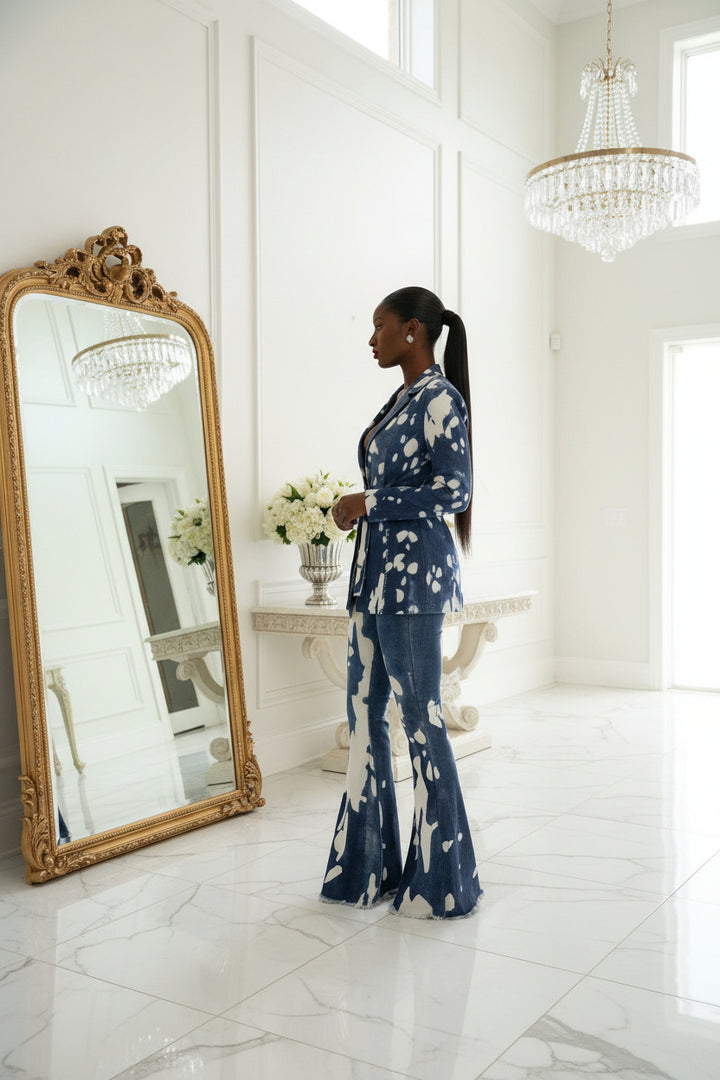 A model wearing a blue and white abstract patterned two-piece set consisting of a long-sleeve blazer and matching flared pants, posed against a light gray studio background.