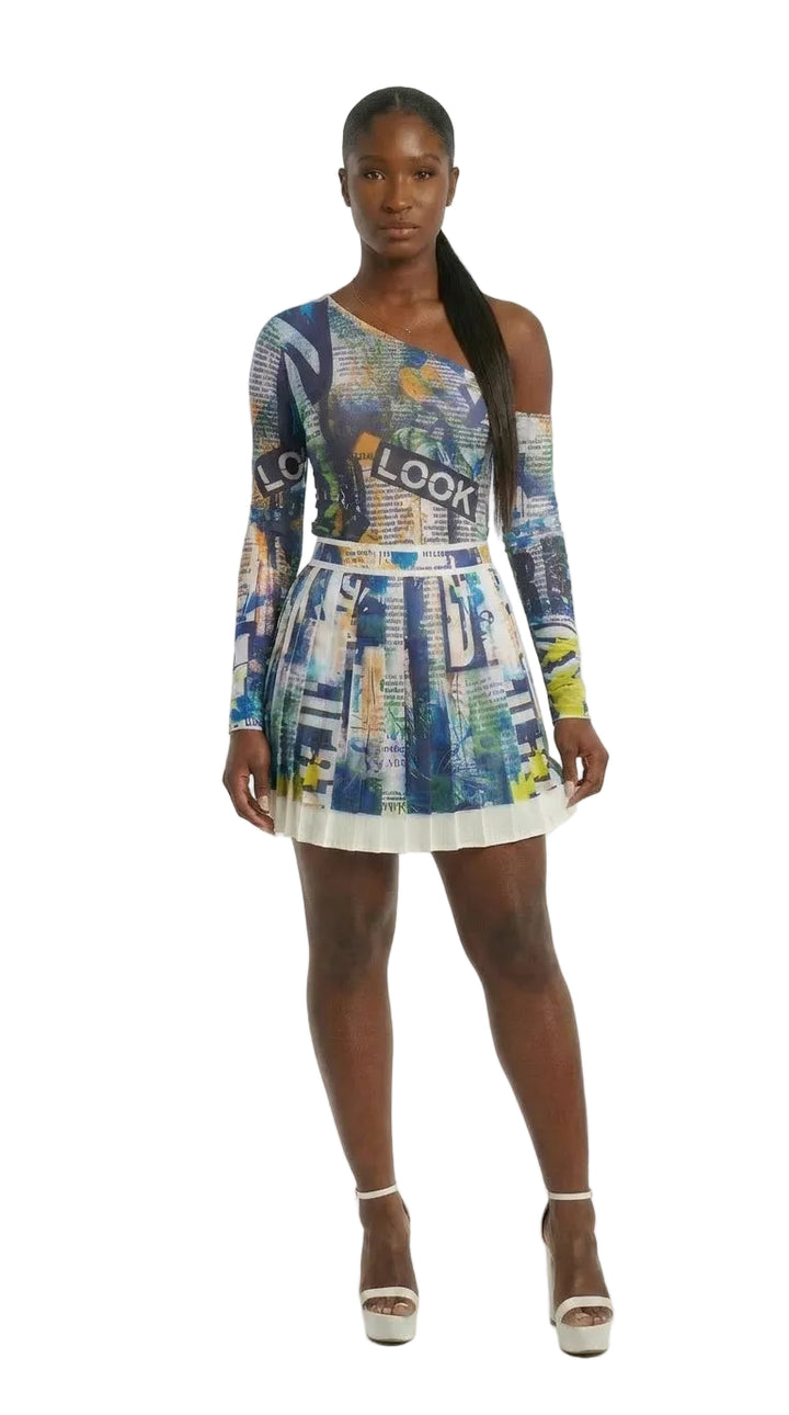 A model wearing a long-sleeve mini dress with a colorful cityscape print in shades of blue, white, and yellow, paired with white platform sandals, against a plain white studio background.