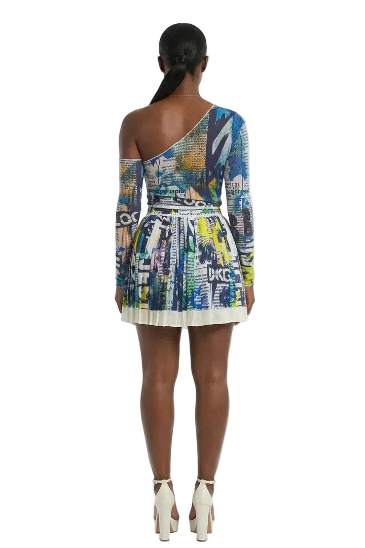 A model shown from the back wearing a one-shoulder mini dress with a colorful graffiti-style print and white high heels, set against a plain white studio background.