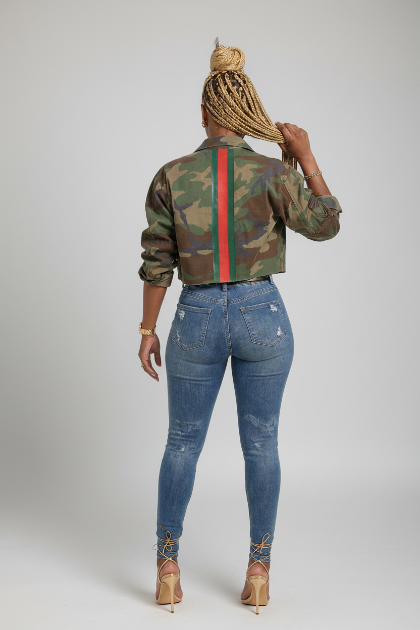 A woman shown from the back wearing a cropped camouflage jacket with a vertical green and red stripe, blue jeans, and lace-up heels against a plain white background.